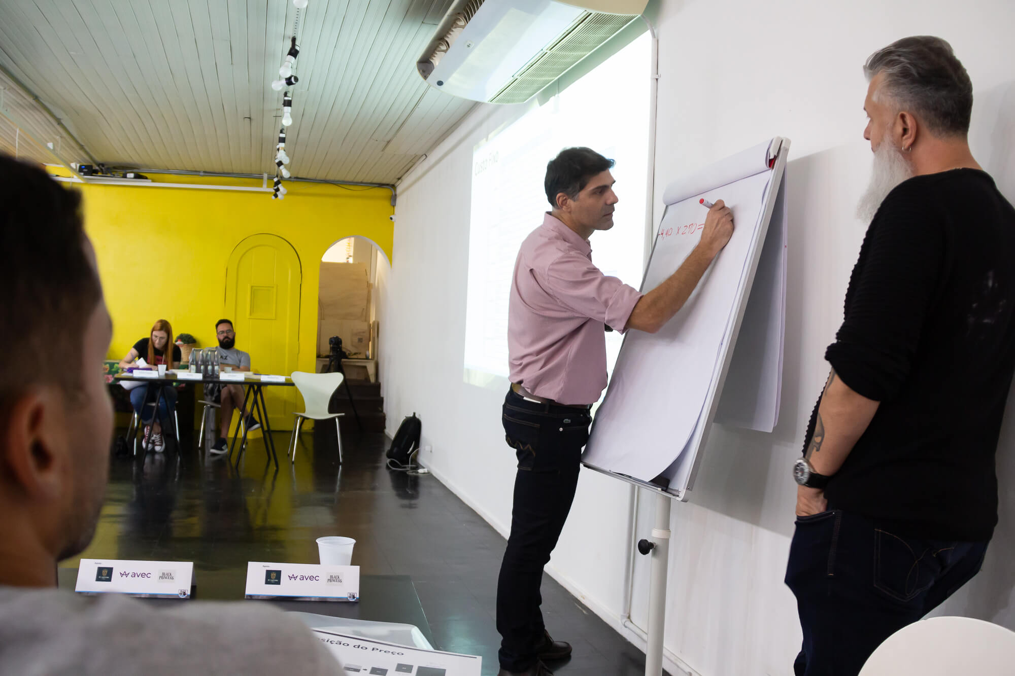 Equipe reunida em sala de reunião enquanto um profissional anota o planejamento no flipchart.