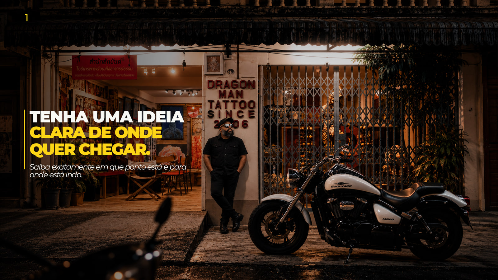 Retrato de Dennis Phillipps encostado na fachada de um estúdio de tatuagem, ao lado de uma moto, com a frase “Tenha uma ideia clara de onde quer chegar”.