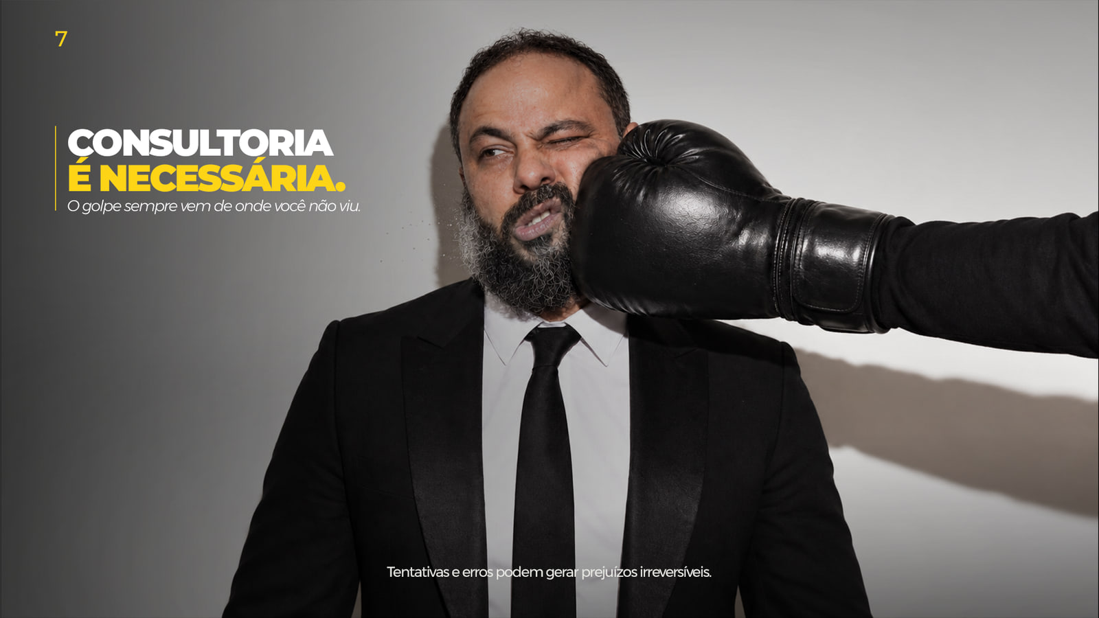 Dennis Phillipps de terno recebendo um golpe de luva de boxe vindo de fora do quadro, com a frase “Consultoria é necessária”.