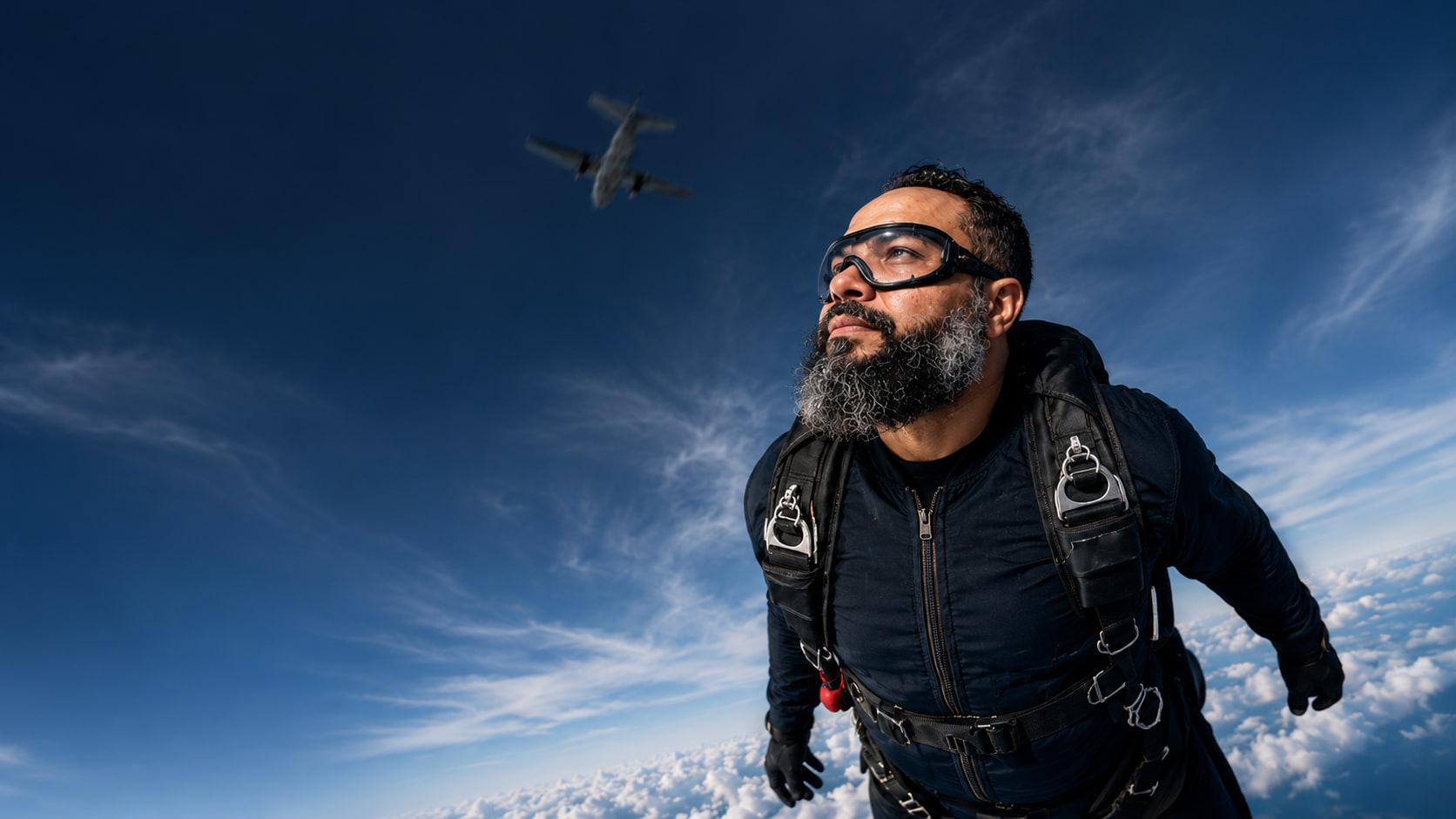 Homem em queda livre de paraquedas olhando para cima, em direção ao avião que se afasta no céu azul.